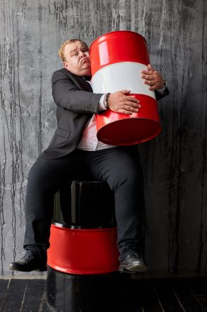 handsome rich caucasian businessman in suit with oil barrel. man sit hugging barrel of oil. business on the extraction of natural resources